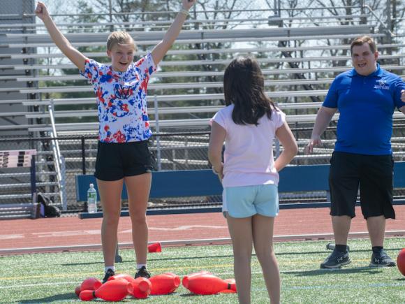 Two girls play sports, one older with her hands in the air celebrating while the younger girl smiles.