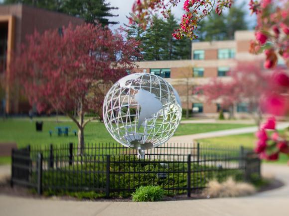 Globe sculpture on the campus green framed by spring blossoms