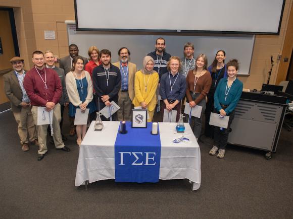 A group of students smiling and the symbol for Gamma Sigma Epsilon in front of them on a table.