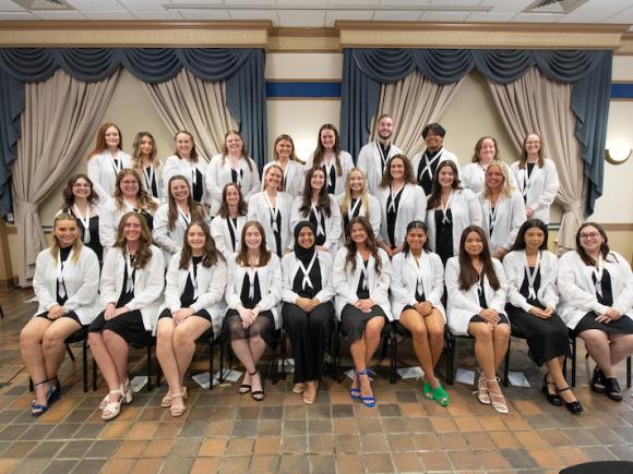 Graduating nursing students in their white coats pose for the camera.