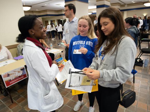 Three students are smiling and hold notebooks in their hand.