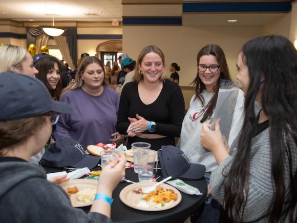 Students surround a table with food, smiling at each other.