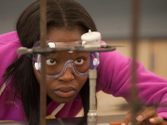 A student wearing protective goggles closely monitors a laboratory experiment.