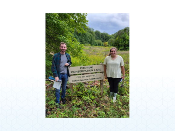 Two WSU students (Michael Heinz, Abigail Mahoney, from left to right) smile and pose in front of a scene which reads "Pitoniak Conversation Land".