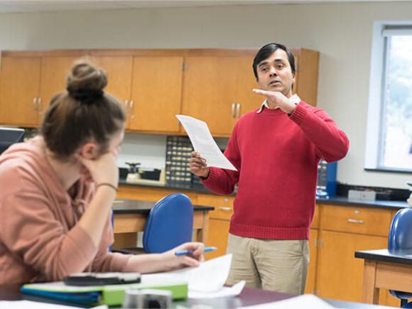 A student seated in a classroom setting listens to a professor.