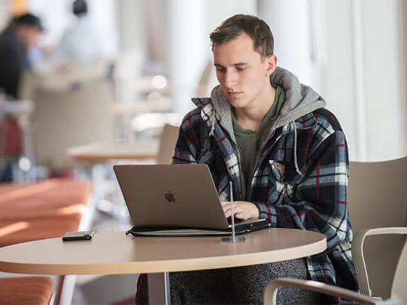 A student works on their laptop in a lounge area.
