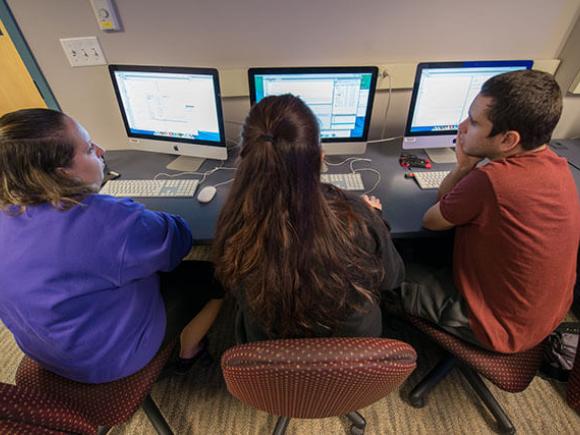 Three students collaborate while working in a computer lab.