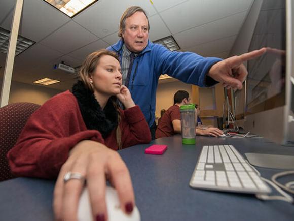  A professor points to something on a student’s computer screen.