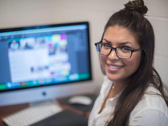 A student smiles while working on a computer.