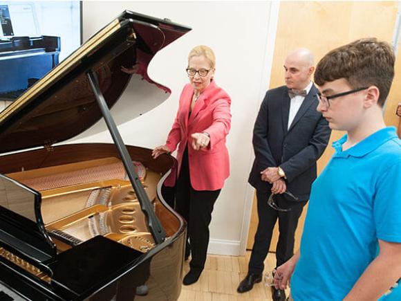 An instructor points at part of a grand piano while instructing students.