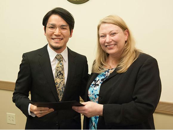 A faculty member hands a student a folder while posing for a picture.