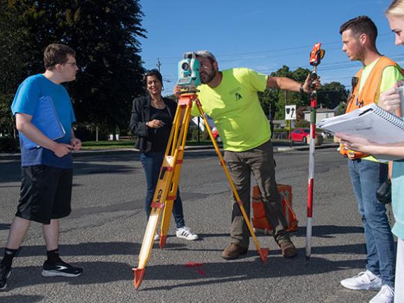 Multiple students observe how to use surveyor equipment.