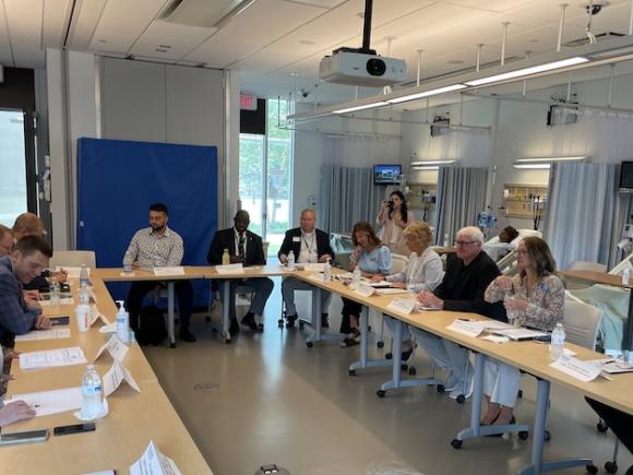 Massachusetts Department of Mental Health Commissioner Brooke Doyle, state Sen. John Velis, and state Rep. Kelly Pease, among other faculty members sit around a rectangular-shaped table with paper in front of them.