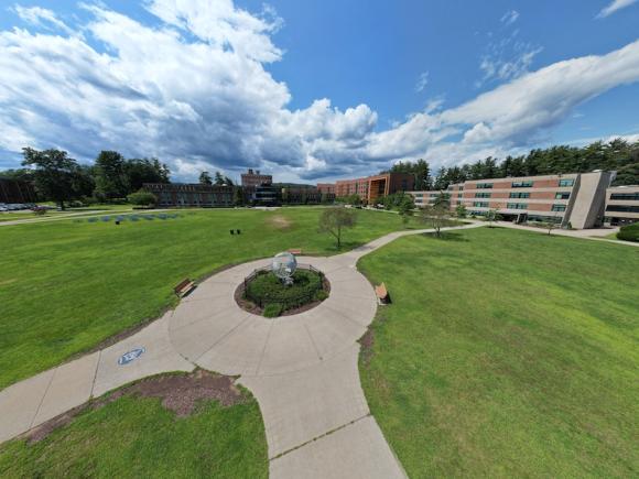 An overhead shot of the campus globe backed by a cloudy, blue sky and greenery below.
