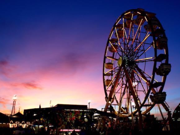 A photo of the sky, colored purple, pink, and yellow, with a silhouetted Ferris wheel in-frame.