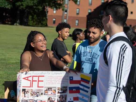 Students gathered around a "Latinx" poster, one with dark hair and glasses, one in a blue t-shirt, and another in a long, white sleeved t-shirt.