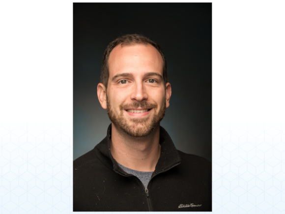 Robert Chatt, a white-skinned man with short brown hair and a beard smiles and wears a black sweater.