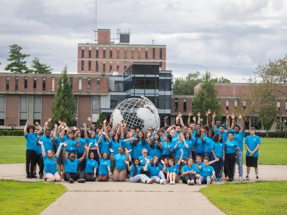 Urban Education group photo in front of campus globe with students wearing blue tee shirts.