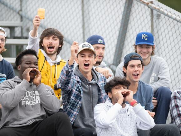 Students cheer on the bleachers during the Homecoming football and soccer games. They're yelling, and some have fists in the air.