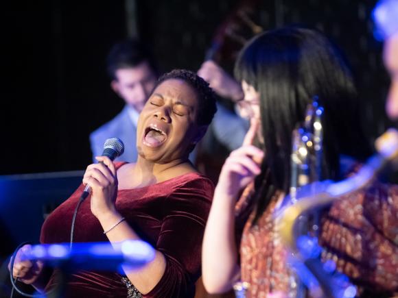 Jazz singer with microphone wearing red performing with band.