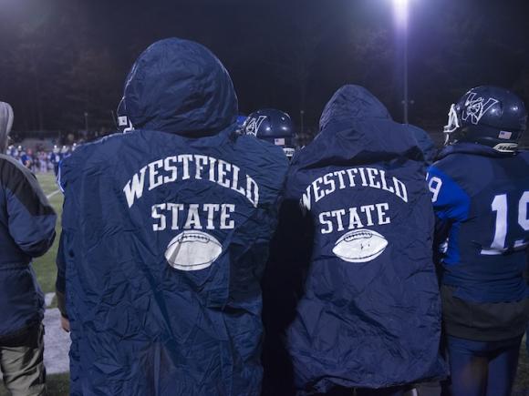 Two students in navy-blue Westfield State ponchos during a rainy football game.