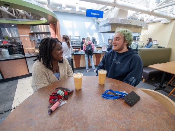 Dining services two students smiling and chatting at table with ice coffees.