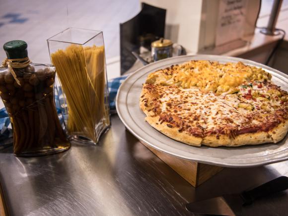 Cheese pizza with pasta and olive oil in back of it.