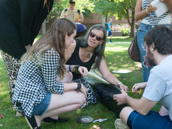 Math class visit outside with professor in a small group with two students showing them a measurement.