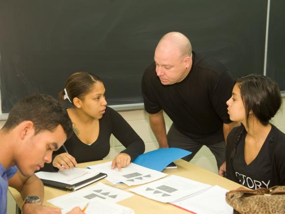 Math professor working with a small group of three students who are working on a math assignment.