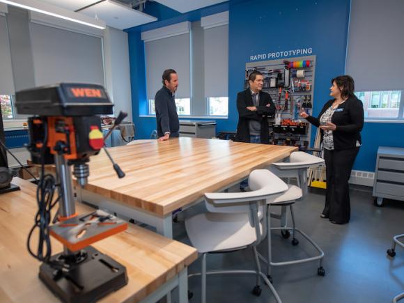 The new Research, Innovation, Design, and Entrepreneurial (RIDE) Center, with wooden tables, white chairs, blue walls, and three members of the Beveridge Foundation.