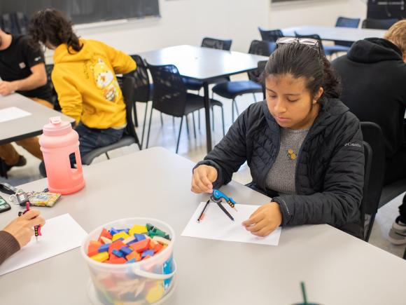 Student in math class wearing a black coat and holding a pen.