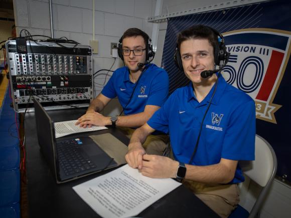 Brayden Cutler and Zachary Bianco broadcasting intramural events on campus. They wear blue polos and black headsets, which they use to do play-by-play commentary for sports games at the University.