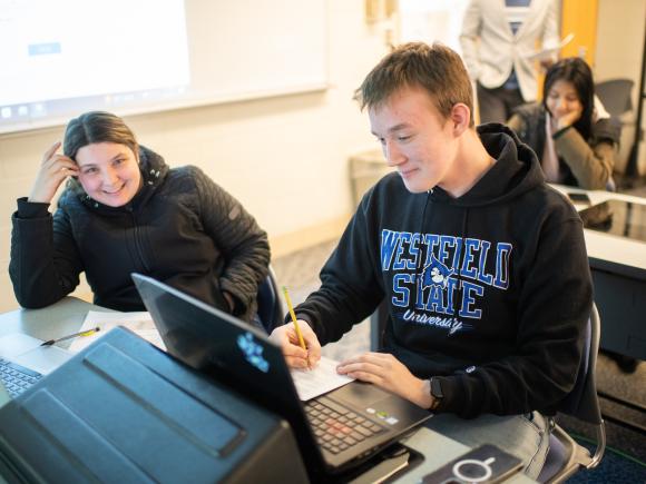 Two CIS students in front of a lap top smiling. One wearing black coat the other a WSU sweatshirt.