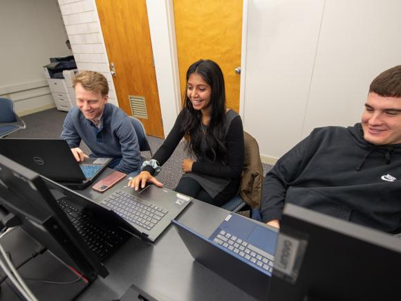 Three computer science students smiling in front of laptops.
