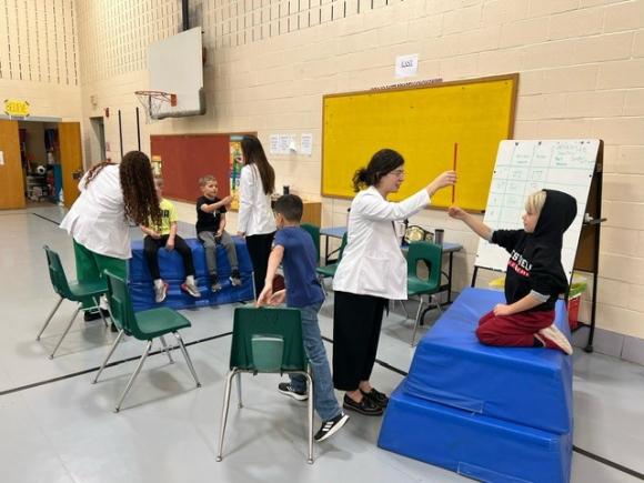 Physician assistant majors from WSU use pallets to show kids from Paper Mill Elementary School what reflexes are.