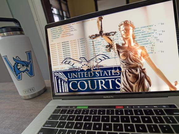Montage image of a white water tumbler with a blue Westfield State University logo next to a laptop on a desk showing an image of computer code, a statue of the scales of justice and the logo for the United States Courts system.