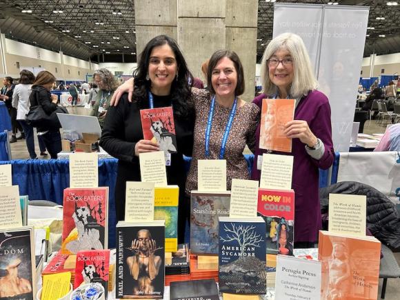 Carolina Hotchandani, a Latinx and South Asian poet, Rebecca Olander, Visiting Lecturer at Westfield State, Catherine Anderson, an older white-haired woman standing together at a booth full of poetry books. They are at the Association of Writers & Writing Programs conference.