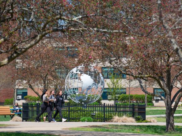 Campus globe in the spring with flowering trees and three students walking in front of it.