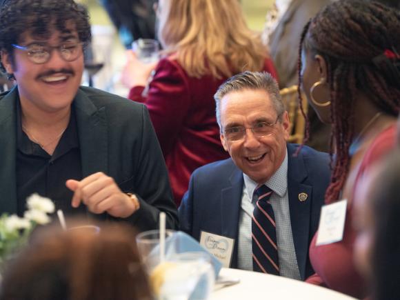 Mayor Michael McCabe of Westfield conversing with students at last week's Keeper of the Dream dinner. He kneels at a white-clothed table and wears a blue coat jacket, light blue shirt, and maroon-striped tie.