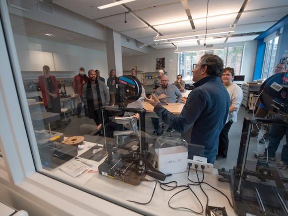 Faculty and staff gather at the RIDE Center as part of a two-day workshop on the new technology. They gather around a laser printer, 3D printer, and various other tools that will help enhance classroom work.