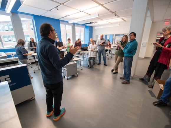 Faculty and staff gather to hear Anna Young and Jose Gomez-Marquez of MakerHealth discuss how to implement the technology at the RIDE Center as part of their academic courses. They listen to Jose and stand in front of various devices such as laser printers, 3D printers, and more.