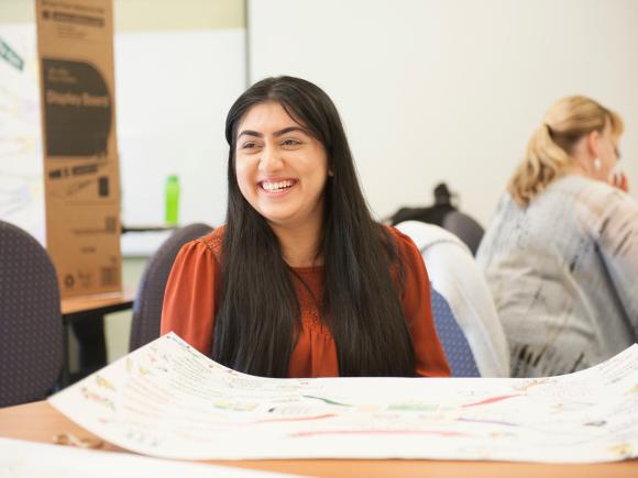 Master of Education student in classroom with long dark hair smiling wearing orange shirt.