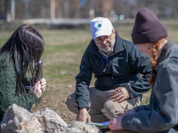 Two students in Earth System Science lab looking at a rock with a faculty member.