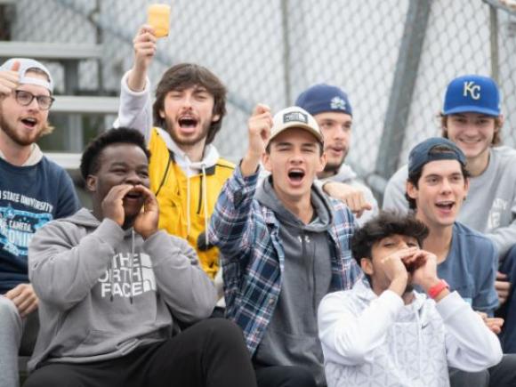 A group of students cheer while seated in the stands at a sporting event.