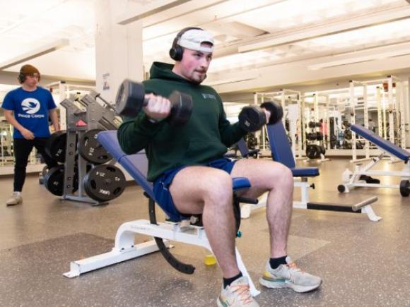 A student lifts weights while seated on a weight bench in one of Westfield State University’s fitness facilities.
