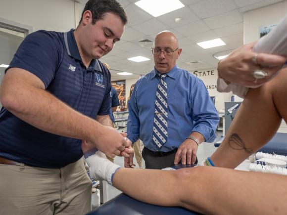 Student practicing ankle taping techniques with faculty guidance.
