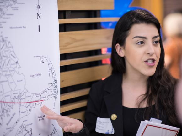 Thalita Neves speaks with an attendee while presenting beside a map of Massachusetts at a campus event.