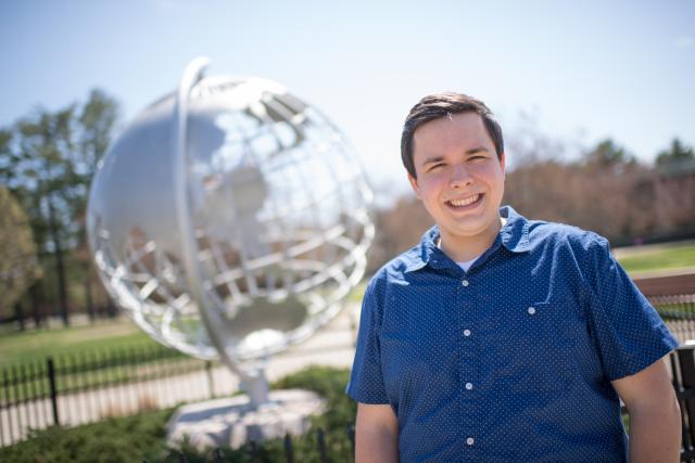 Photo of Aaron Lessing in front of the Globe sculpture one the campus green