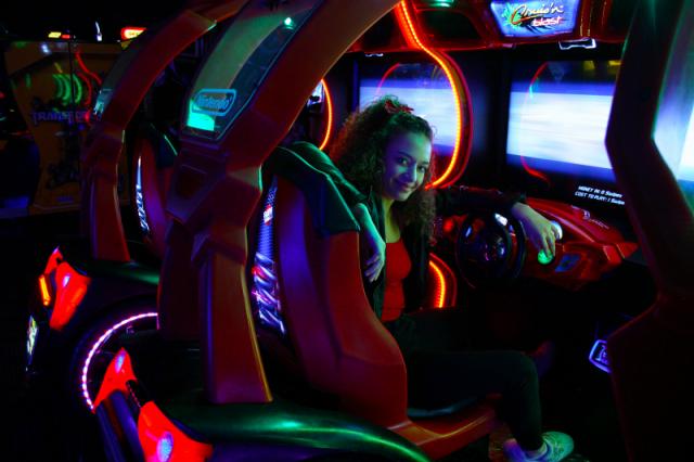 Image of a young female sitting in an arcade driving simulator