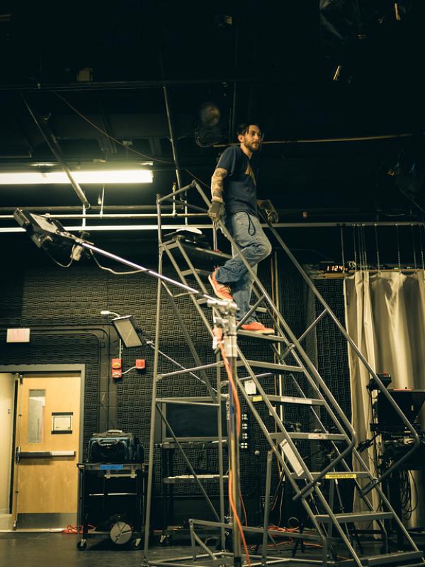 Male student walks down a studio ladder in the lighting lab in the Dower Center for the Arts